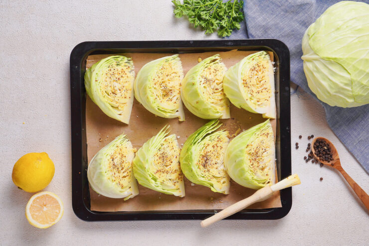 Eight cabbage wedges are placed on brown paper on a baking tray.