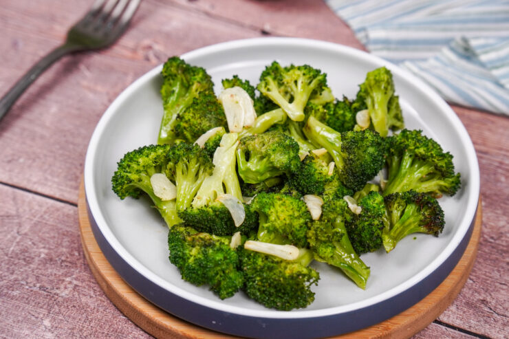 A white plate containing roasted broccoli with olive oil, sliced garlic and salt and pepper.