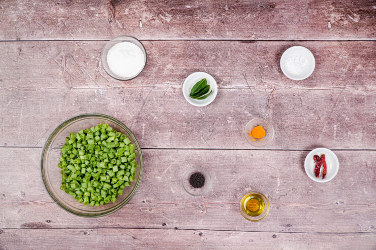 Overhead shot of the ingredients needed to make string beans and coconut stir fry including chopped string beans, shredded coconut, black mustard seeds, dried red chili peppers, turmeric, and olive oil.