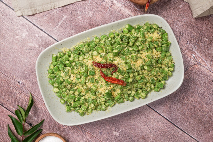 Overhead shot of a rectangular white bowl filled with string beans and coconut stir fry, and two dried red chili peppers on top. The beans are sliced into bite-sized pieces and the shredded coconut adorns everything.