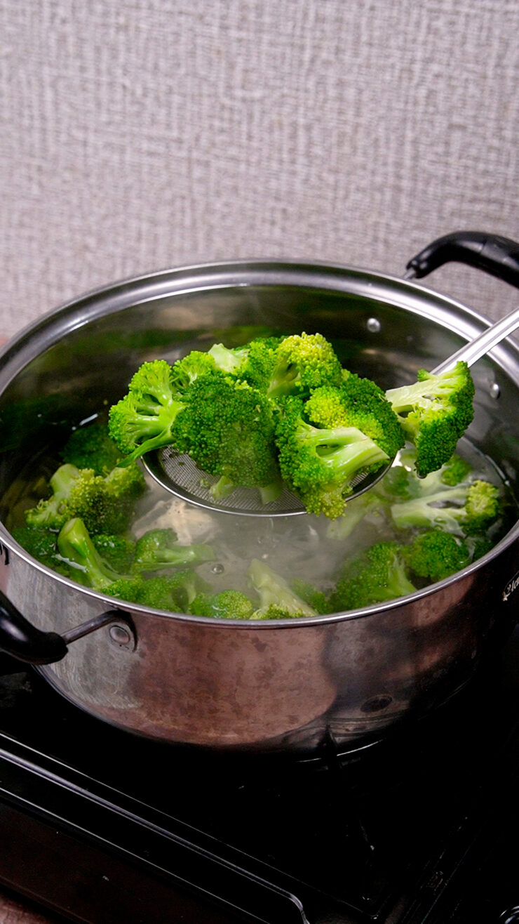 A ladle pulls broccoli florets out of a boiling pot.