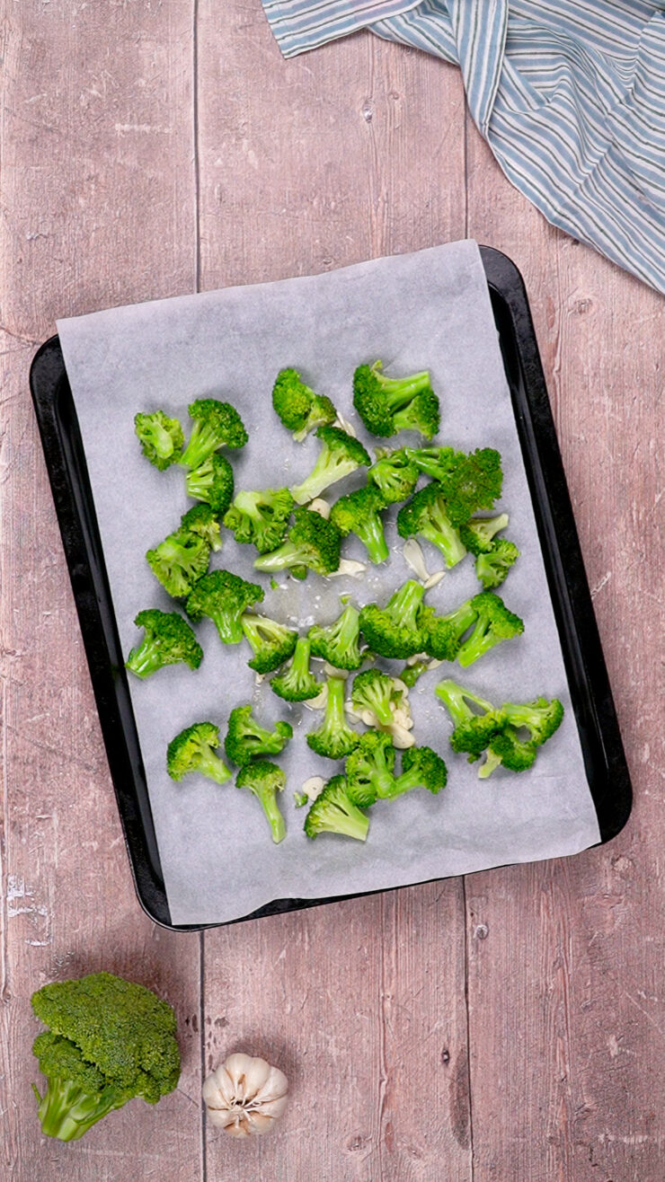 Roasted broccoli with garlic and olive oil arranged on a pan lined with parchment paper.