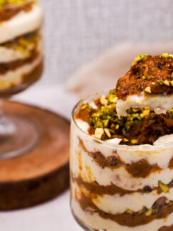 Two tall dessert glasses of carrot halwa trifle with a spoon dipping into one of them. You can see the layers of the carrot mixture and cream mixture in the glasses.