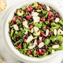 White bowl filled with pomegranate salad with cucumber, black lentils, and pomegranate arils on top.