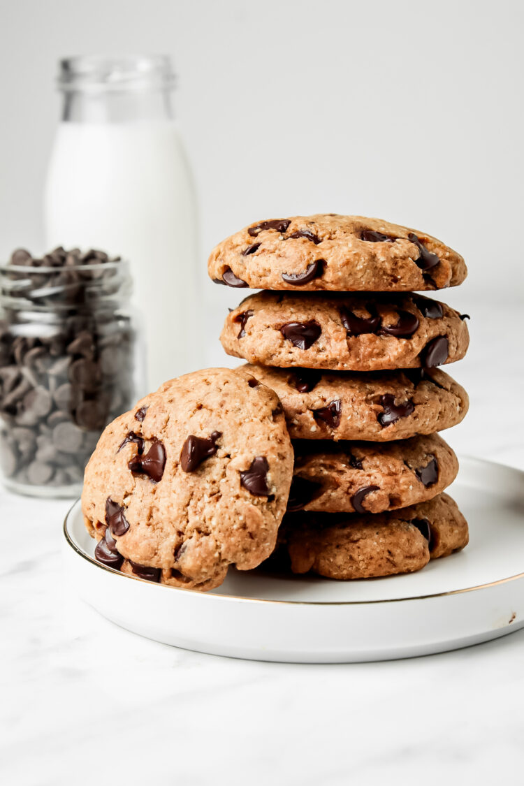Stack of 5 chocolate chip cookies on a plate with another cookie leaning against the cookie tower.