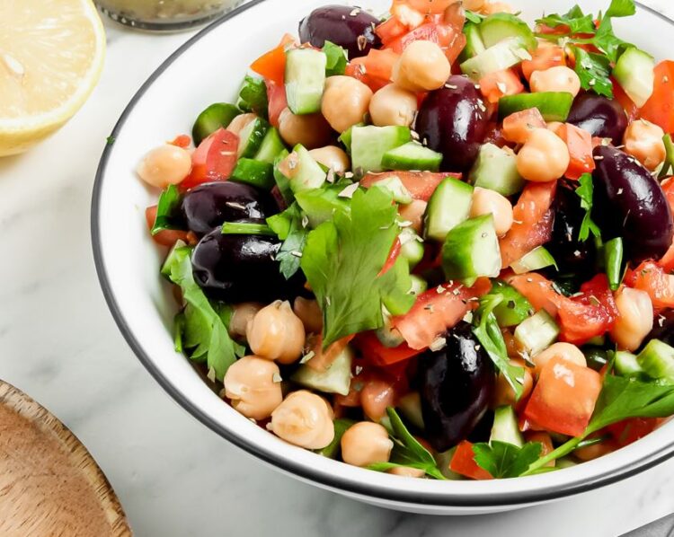 Bowl full of Greek chickpea salad that is studded with black olives and tomatoes, and garnished with herbs.