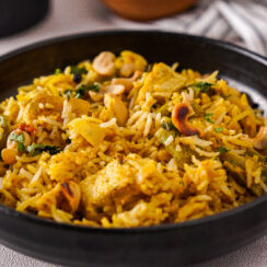 Black bowl filled with Delhi-style biryani which is yellow and studded with vegetables and nuts