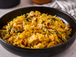 Black bowl filled with Delhi-style biryani which is yellow and studded with vegetables and nuts