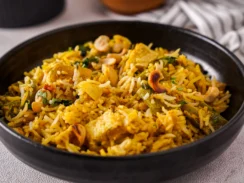 Black bowl filled with Delhi-style biryani which is yellow and studded with vegetables and nuts