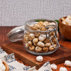 Jar of spiced masala makhana on top of a wooden board with a wooden bowl of makhana behind it
