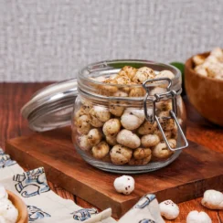 Jar of spiced masala makhana on top of a wooden board with a wooden bowl of makhana behind it