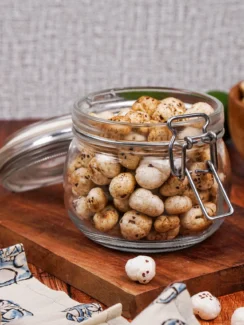 Jar of spiced masala makhana on top of a wooden board with a wooden bowl of makhana behind it