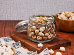 Jar of spiced masala makhana on top of a wooden board with a wooden bowl of makhana behind it