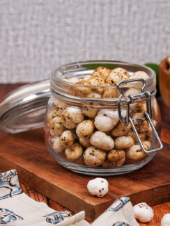 Jar of spiced masala makhana on top of a wooden board with a wooden bowl of makhana behind it