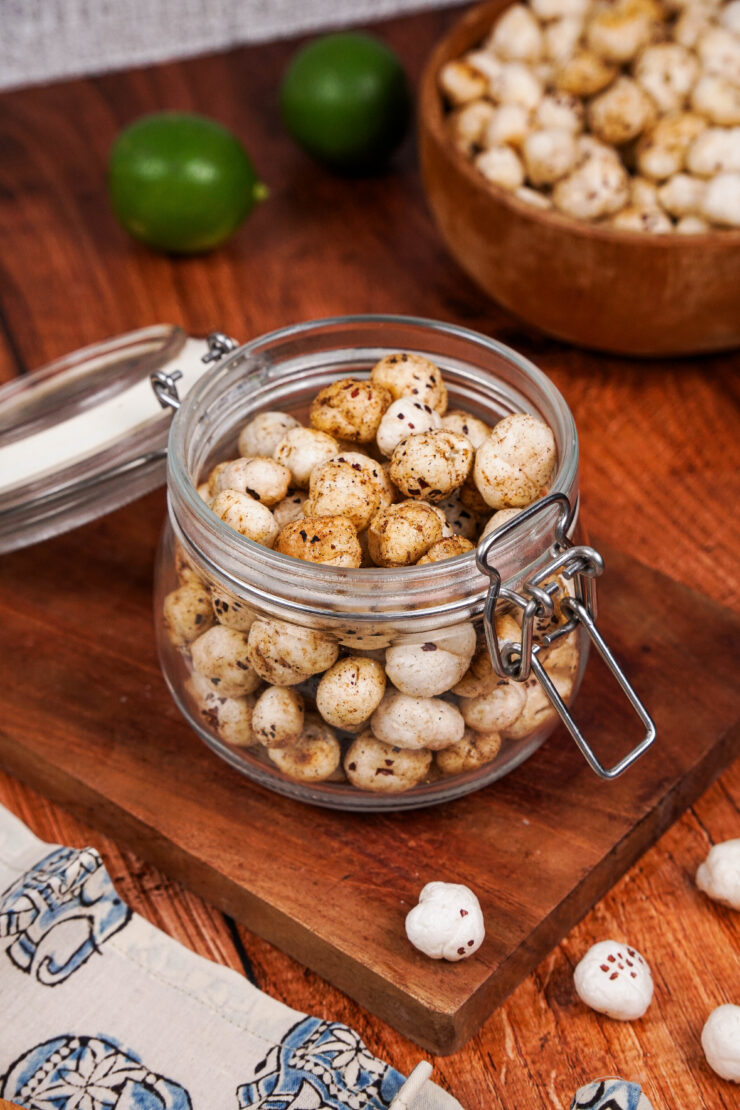 Jar filled with spiced masala makhana sitting on top of a wooden board