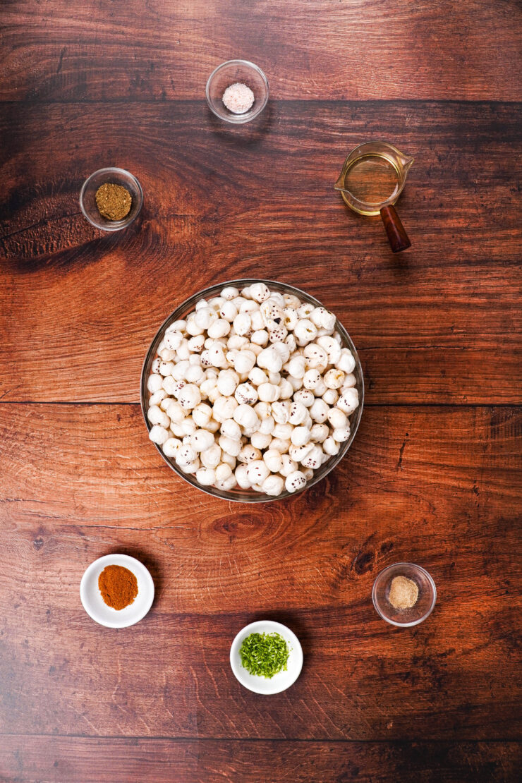 Overhead shot of a large bowl of makhana and smaller bowls of seasonings surrounding it