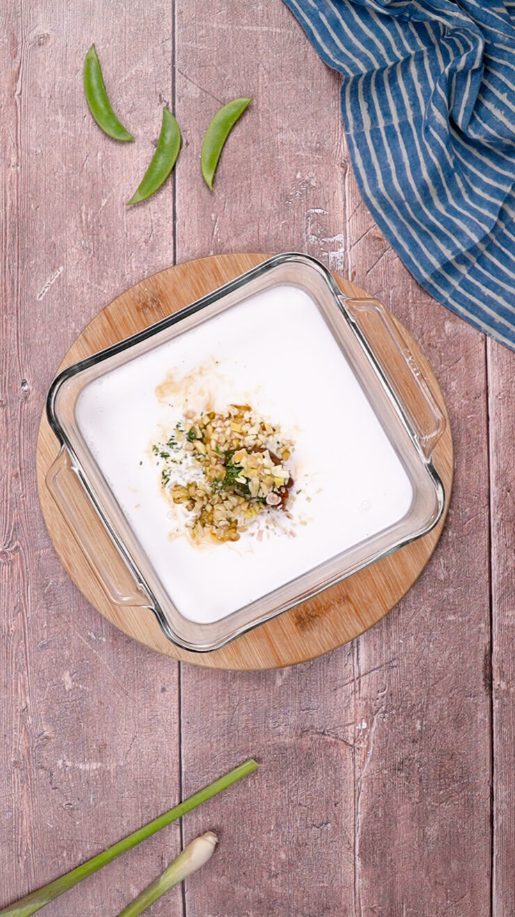 Coconut milk added to the dumpling bake recipe in a glass baking dish.