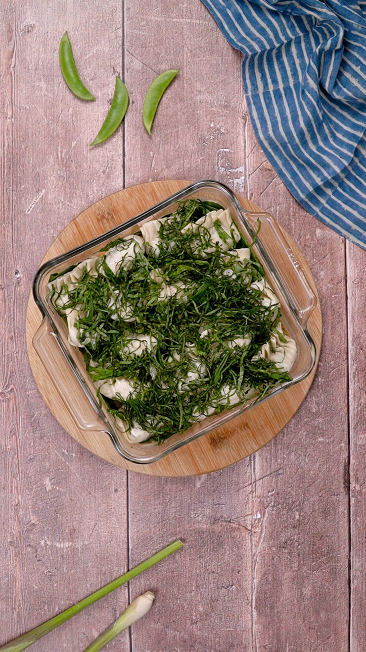 Ingredients for the dumpling bake recipe combined in a glass baking dish, including cilantro.