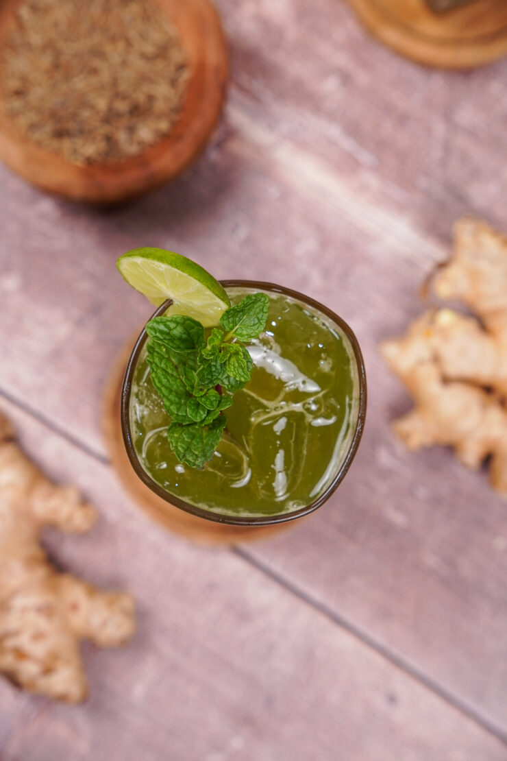 Overhead shot of a tall glass of jaljeera with a lime slice on the glass and mint sitting on top of the drink.